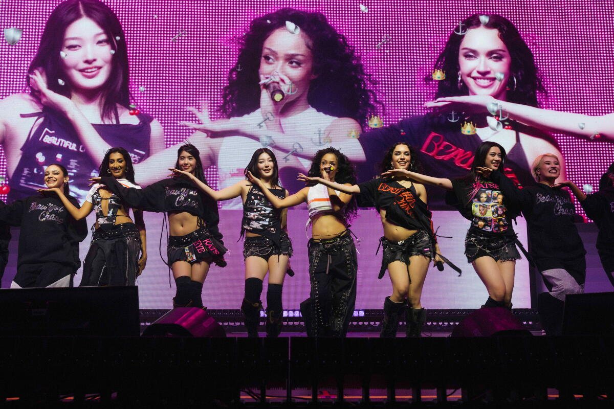 Six performers dancing on stage in front of a large LED screen showing close-ups of the group